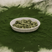bowl of chlorella tablets surrounded by green chlorella powder on a table